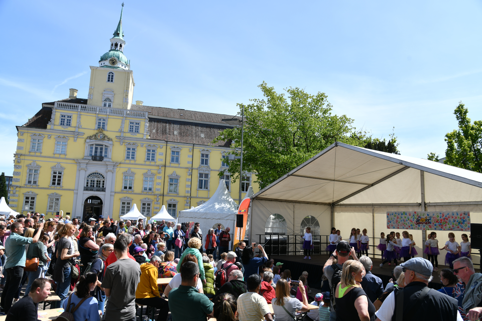 Auf dem Oldenburger Schlossplatz gucken viele Personen Kindern auf einer Bühne beim Tanzen zu.