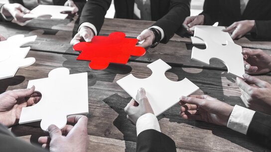 Hände von Geschäftsleuten halten Puzzle-Stücke, darunter ein rotes Teil, das hervorsticht.