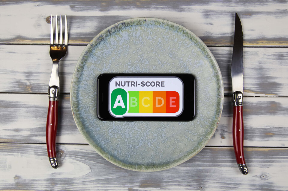 Smartphone mit Nutri-Score A auf einem Teller, umgeben von einem Messer und einer Gabel.
