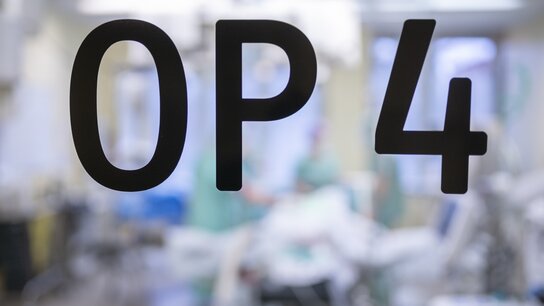 Sicht auf die Glastür mit der Aufschrift „OP 4“ und verschwommener Hintergrund einer chirurgischen Umgebung.