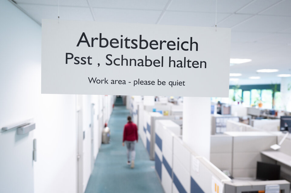 Blick durch eine Tür in ein weiß gehaltenes Großraumbüro. An der Tür hängt ein Schild mit der Auftritt "Arbeitsbereich Psst, Schnabel halten"
