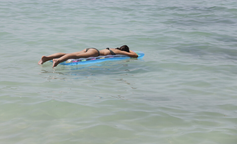 Person in einem schwarzen Bikini liegt auf einem Luftmatratze im seichten Wasser einer Küste.