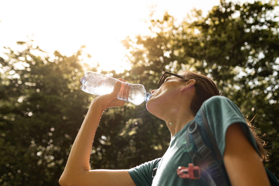 Junge Person trinkt Wasser aus einer Flasche, umgeben von Bäumen, im Sonnenlicht.