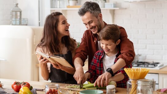 Familie kocht zusammen in einer modernen Küche, während sie gemeinsam an einem Rezept arbeiten und viel Spaß haben.