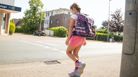 Ein Mädchen mit Rucksack und Shorts geht auf dem Bürgersteig in einer Wohngegend.