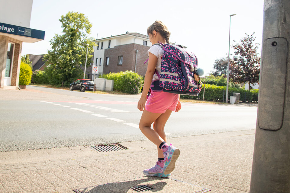Ein Mädchen mit Rucksack und Shorts geht auf dem Bürgersteig in einer Wohngegend.