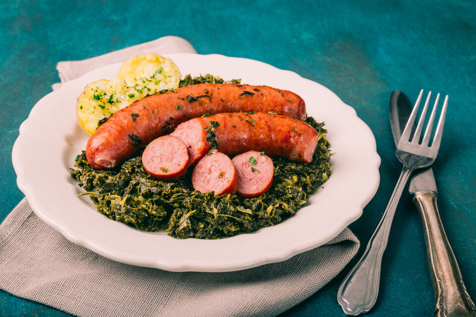 Zwei Bratwürste auf einer Portion Grünkohl, garniert mit Scheiben von Wurst und Beilagen.