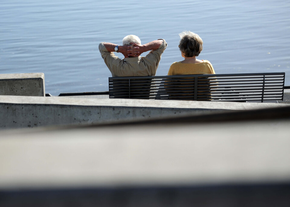 Ein älteres Paar sitzt entspannt auf einer Bank am Wasser und genießt den Ausblick.