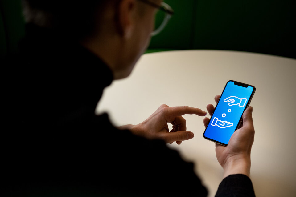 Person hält Smartphone, auf dem ein grafisches Symbol zweier Hände und einer Münze angezeigt wird.