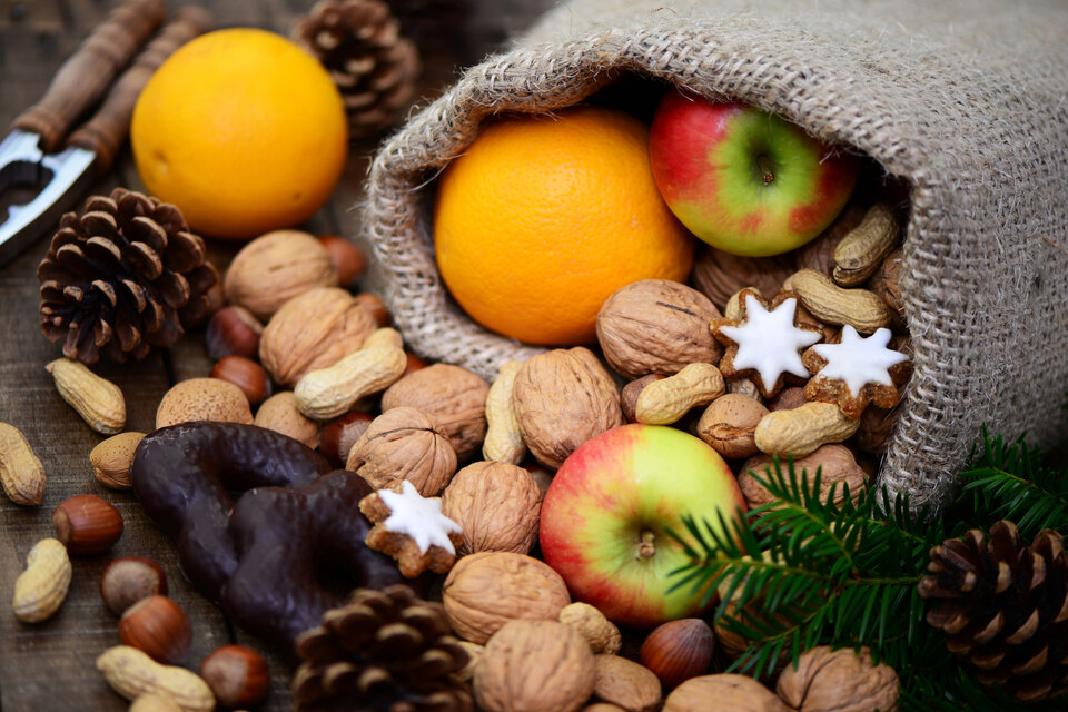 Geschenksack mit Äpfeln, Orangen, Nüssen, Lebkuchen und Tannenzweigen auf einer Holzoberfläche.