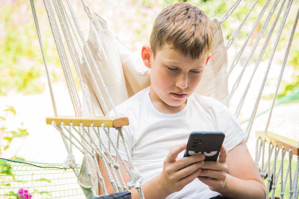 Junge sitzt in Schaukel und guck auf Handy