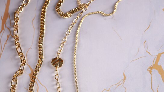 Mehrere goldene Halsketten liegen über einem marmorierten Hintergrund in sanften Beigetönen.