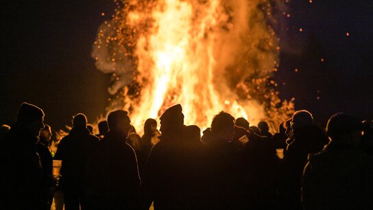 Ein Osterfeuer bei Nach vor dem viele Personen stehen und sich unterhalten.