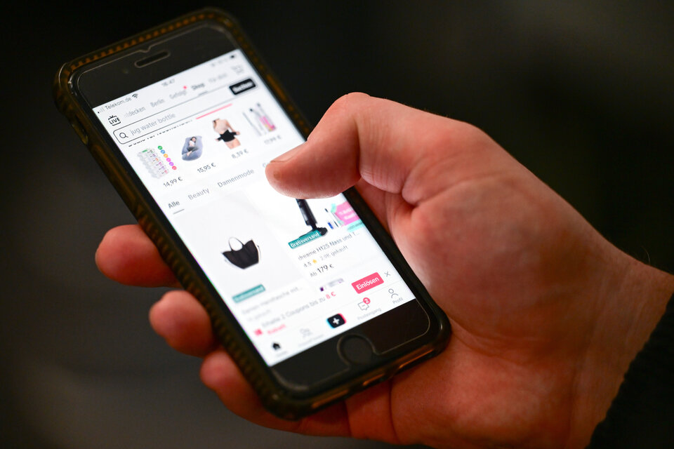 Ein Hand hält ein Smartphone, auf dem eine Shopping-App mit verschiedenen Produkten angezeigt wird.