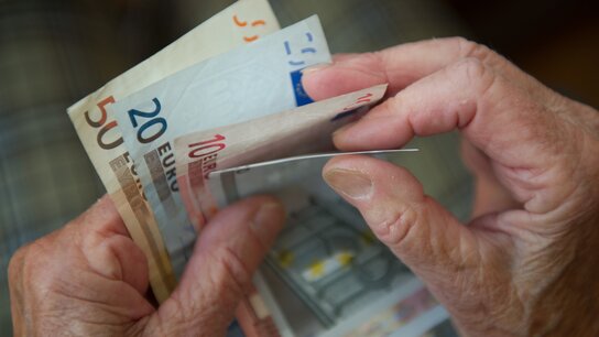 Fingernägel halten mehrere Euro-Scheine in verschiedenen Stückelungen, während eine andere Hand den Geldschein faltet.