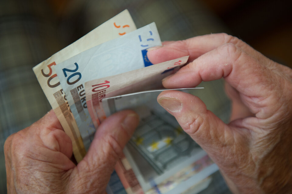 Fingernägel halten mehrere Euro-Scheine in verschiedenen Stückelungen, während eine andere Hand den Geldschein faltet.