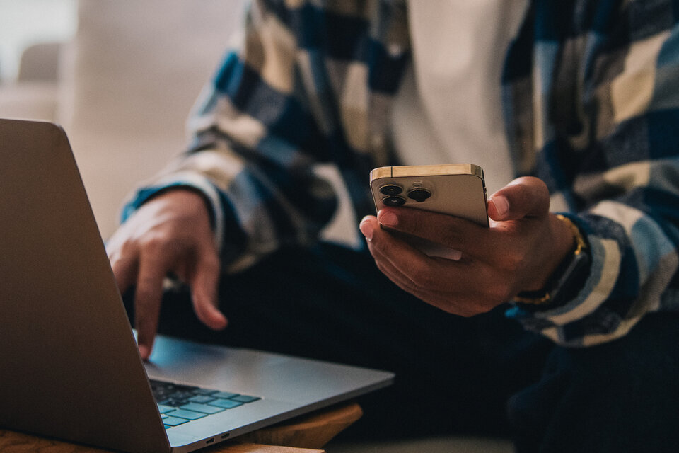 Person sitzt mit Laptop und Smartphone in der Hand, während er auf der Couch arbeitet.
