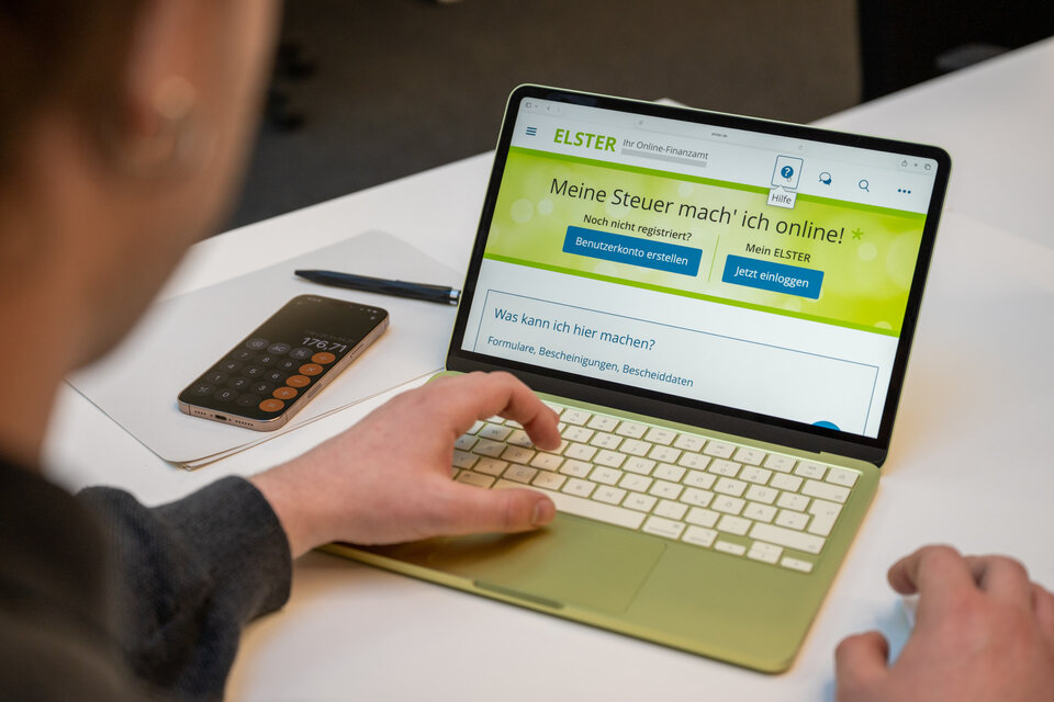 Arbeiter nutzt ein Laptop, um die ELSTER-Website für Online-Steuerverwaltung zu besuchen. Neben ihm liegt ein Taschenrechner.