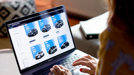 Eine Person betrachtet auf einem Laptop eine Website mit verschiedenen Autowerbungen und Preisangaben.