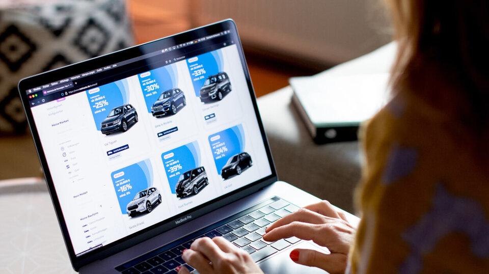 Eine Person betrachtet auf einem Laptop eine Website mit verschiedenen Autowerbungen und Preisangaben.