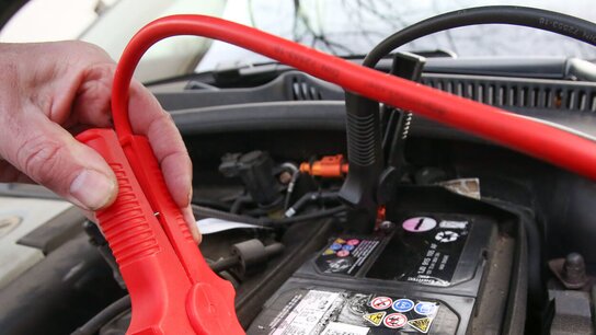 Eine Hand hält ein rotes Kabel, das an einem Autostarter-Batterieanschluss angeschlossen ist.