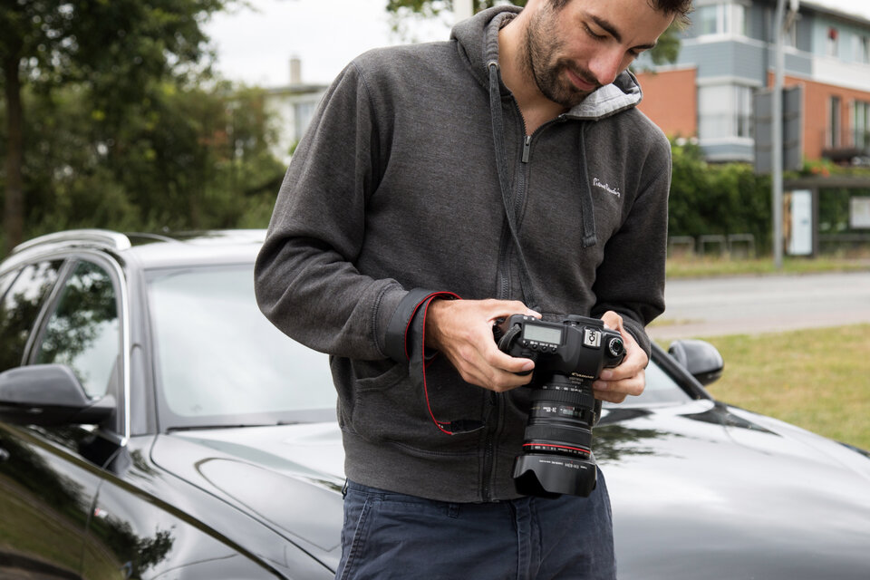 Mann hält eine Kamera in den Händen, steht neben einem schwarzen Auto, konzentriert auf das Display der Kamera.