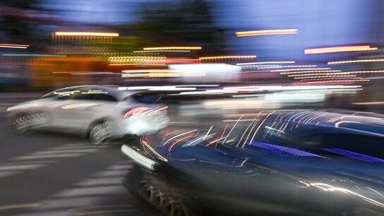 Ein unscharfes Bild von zwei Auto, die im Halbdunkeln nebeneinander abbiegen.