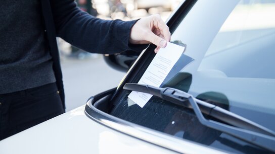 An ein parkendes Auto wird ein Strafzettel gehängt.