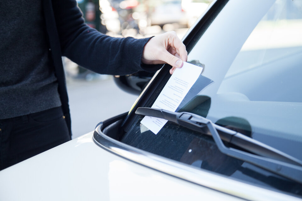 An ein parkendes Auto wird ein Strafzettel gehängt.