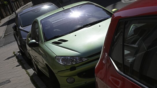 Drei Autos stehen an einer Straße in der Sonne.