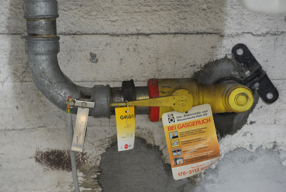 Gasventil mit einer gelben Kennzeichnung, an einer grauen Wand, mit Sicherheitsinformationen und einem Warnhinweis bei Gasgeruch.