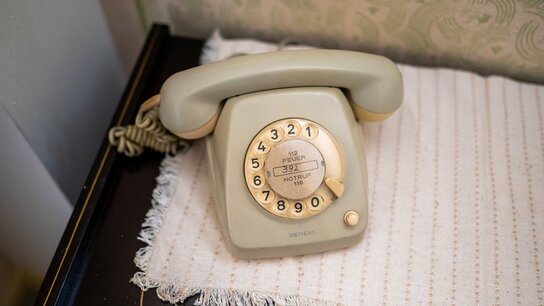 Beige Wählscheibentelefon auf einem Tisch, umgeben von einer gestrickten Unterlage.