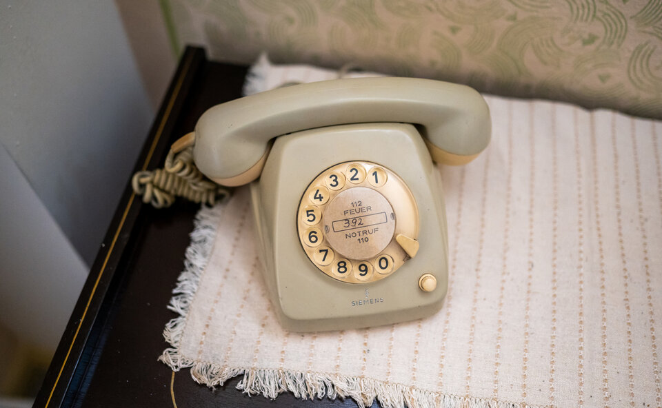 Beige Wählscheibentelefon auf einem Tisch, umgeben von einer gestrickten Unterlage.