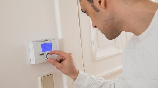 Mann verstellt den Temperaturregler an einer Wand, während er auf das Display sieht.