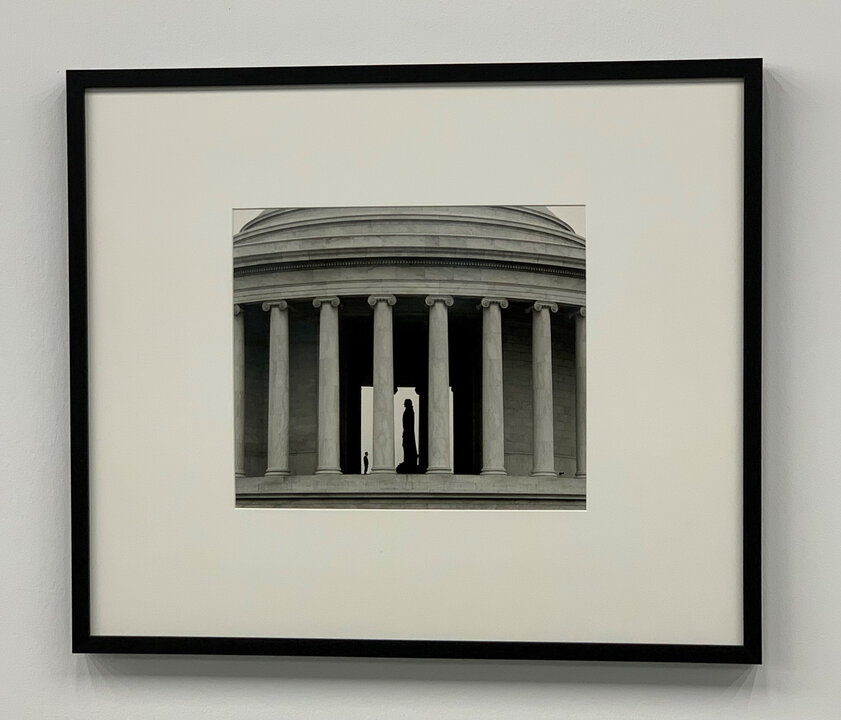 Silhouette einer Person vor architektonischen Säulen in Schwarz-Weiß, mit einer zentralen Öffnung im Gebäude.