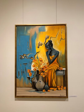 Eine nachdenkliche Frau in orangefarbener Robe sitzt neben einer Vase mit blühenden Blumen vor einer farbigen Wand.