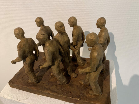 Skulptur von sieben menschlichen Figuren in Bewegung, aus Ton gefertigt, auf einer rechteckigen Basis.