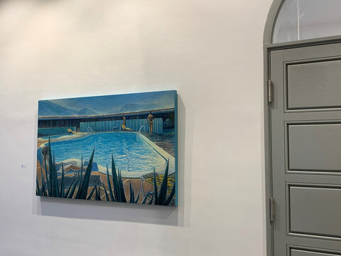 Buntes Gemälde eines Schwimmbeckens mit Liegen und Pflanzen, aufgehängt an einer hellen Wand neben einer grauen Tür.