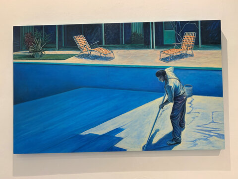 Ein Mann streicht den Boden eines leeren Schwimmbeckens, während Sonnenliegen und Pflanzen im Hintergrund sichtbar sind.