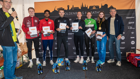 Sechs Sportlerinnen und Sportler mit Urkunden stehen auf einer Bühne bei der Siegerehrung des Goldenbog Marathons.