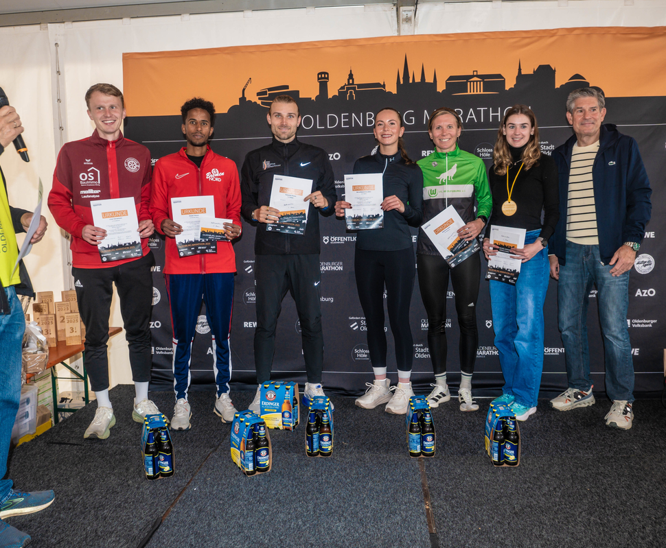 Sechs Sportlerinnen und Sportler mit Urkunden stehen auf einer Bühne bei der Siegerehrung des Goldenbog Marathons.