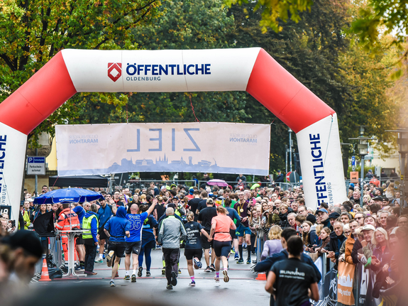 Menschen starten beim Oldenburger Stadtlauf unter einem großen Bogen, mit Menge und Teilnehmern in sportlicher Kleidung.