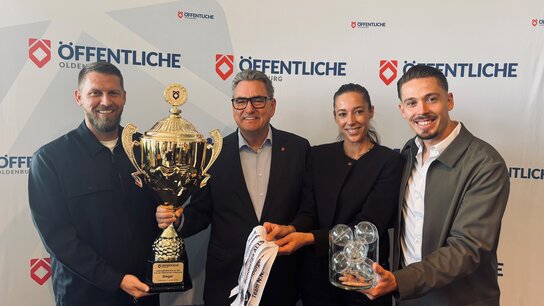 Aaron Hunt (ehemaliger Fußballer und Jürgen Müllender (Vorstandsvorsitzender der Öffentliche Oldenburg) halten einen Pokal, rechts daneben stehen Carina und Fabian Burdenksi