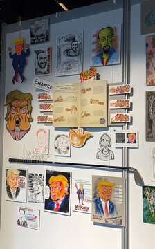 Wand mit verschiedenen Zeichnungen und Karikaturen, vor allem von einer Person mit markanten Gesichtszügen und orangefarbener Haarpracht.