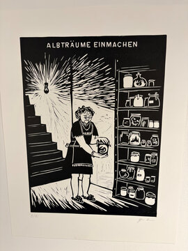 Eine Frau steht vor einem Regal voller Gläser und Konservendosen, während sie ein Gefäß in der Hand hält.