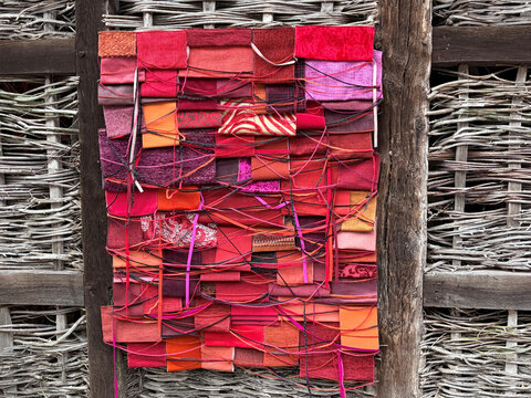 Textilkunstwerk aus roten und pinken Stoffstücken, kunstvoll verflochten und an einer natürlichen Holzstruktur befestigt.