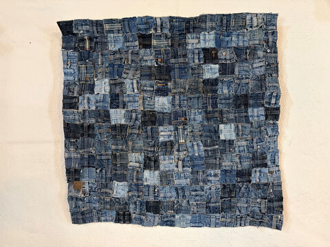 Patchwork aus verschiedenen Jeansstücken in Blau- und Grautönen, an einer Wand aufgehängt.