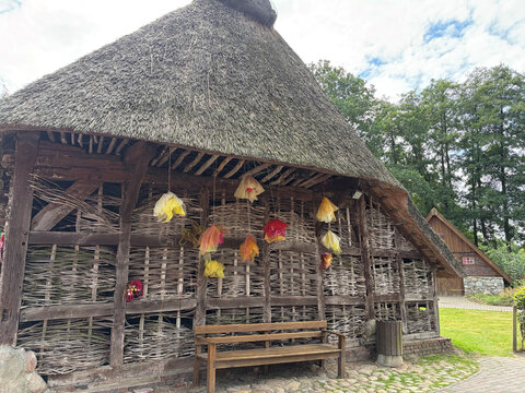 Historisches Fachwerkhaus mit Reetdach, geschmückt mit bunten Stoffen, umgeben von Bäumen und einem gepflasterten Weg.