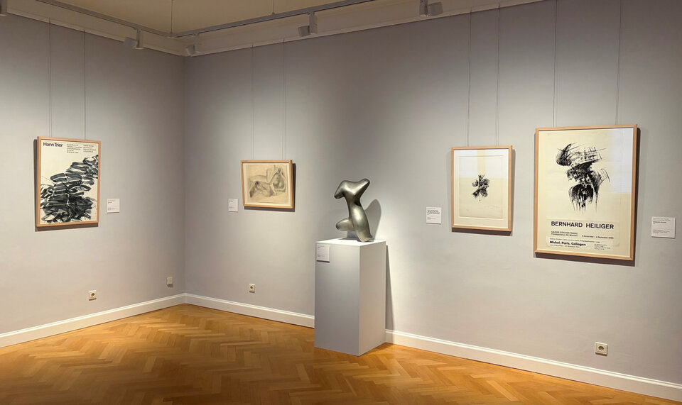 Moderne Kunstgalerie mit mehreren gerahmten Zeichnungen und einer abstrahierten Skulptur auf einem weißen Podest.