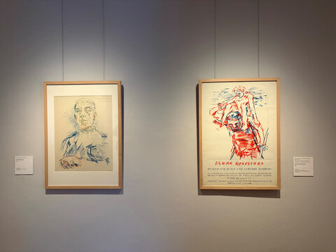 Zwei gerahmte Kunstwerke an einer Wand: links ein Porträt, rechts eine charakteristische Figur in lebendigen Farben.